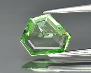 Natural gemstone green zircon in tongs on a gray background