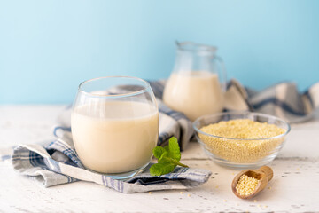 Millet milk in glass, jar and bowl on white wooden table with blue background