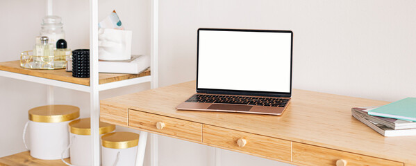 Laptop with blank white screen on office desk interior. Stylish rose gold workplace mockup table view. Panoramic banner