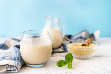 Millet milk in glass, jar and bowl on white wooden table with blue background