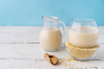 Millet milk in glass, jar and bowl on white wooden table with blue background and copy space