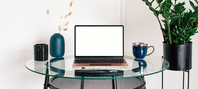 Laptop with blank white screen on office desk interior. Stylish rose gold workplace mockup table view. Panoramic banner