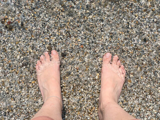 foot of white woman standing in sea with small pebbles in summer