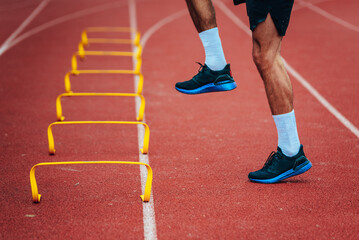 Male runner exercising and jumping on athletic track. Sport photo, warm up, edit space, Yellow obstacles on the red track