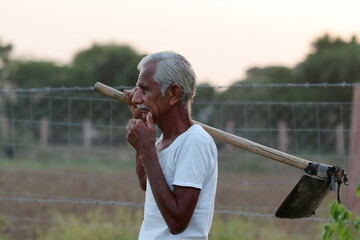 photo of indian aged Farmer holding a shovel in his hand and thinking about something in the field