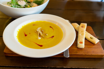 Pumpkin Soup Garnished with Mushrooms  in white plate on wooden table