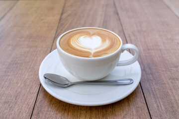 Latte coffee or cappuccino coffee in white cup with beautiful heart shape latte art on wooden table.