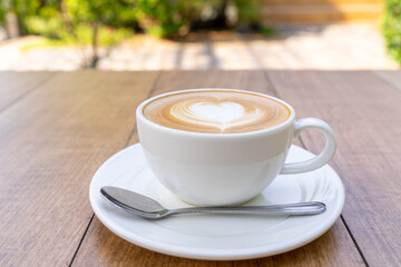 Latte coffee or cappuccino coffee in white cup with beautiful heart shape latte art on wooden table.