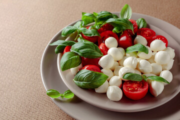 Caprese salad with tomato, mini mozzarella and basil on a brown background.