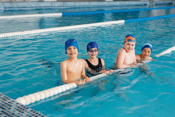 A group of boys and girls play and learn to swim in a modern swimming pool. Development of children's sports. Healthy parenting and promotion of children's sports.