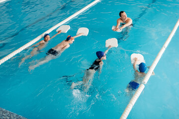 A group of boys and girls train and learn to swim in a modern swimming pool with an instructor....
