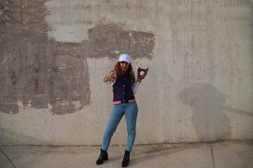 young and beautiful red-haired woman with baseball cap, jacket with baseball bat defying camera....