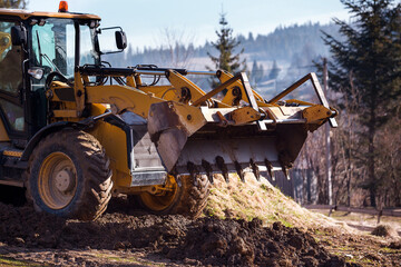 The excavator backfills the pit with the front bucket and moves soil around the construction site. Close-up. Heavy construction equipment © sergiophoto