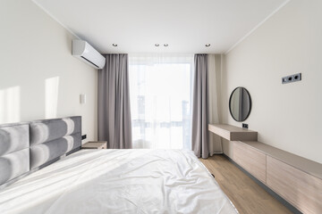 Wide corner of the bedroom in a modern style with a large bed, window, air conditioning and a round...