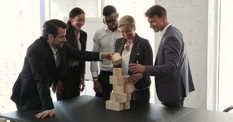 Senior adult woman coach business trainer psychologist provide teambuilding game activity in multiethnic staff group. Motivated diverse mixed race team businesspeople colleagues build tower from cubes