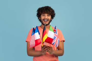 Happy hindu guy holding diverse flags, blue studio background