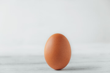 Brown chicken egg stands on wooden table on white background. © AndreyFrol