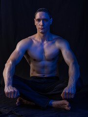 bare-chested man in colored light. showing muscles, posing. Black background.