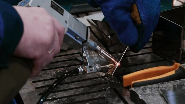 Welder hands using portable handheld laser welding machine with sparks close up view. Metalworking, industrial, equipment, technology and manufacturing concept.