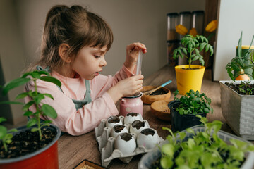 Little girl planting seeds in a eggshells watering it