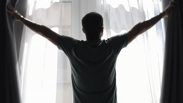 Man opening bedroom curtains to welcome a new day in the morning