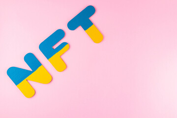 NFT Non-Fungible Token in Ukrainian flag colors. Blue-yellow NFT inscription on pink background. Ukraine support concept. Top view. Copy space