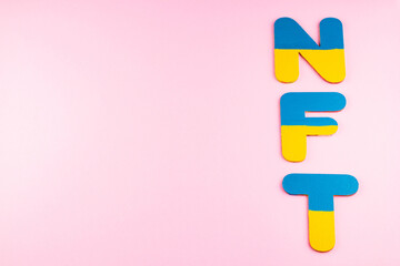 NFT Non-Fungible Token in Ukrainian flag colors. Blue-yellow NFT inscription on pink background. Ukraine support concept. Top view. Copy space