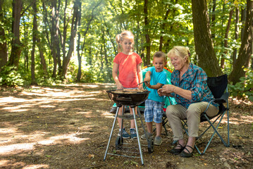 Family picnic concept with grandchildren and grandmother making barbecue