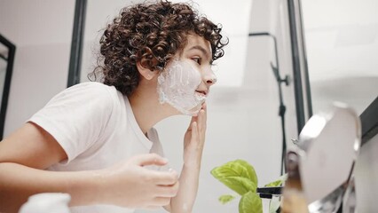 Cute boy with curly hair smears shaving cream on face
