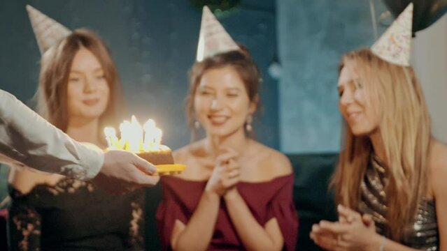 Young woman blowing out fire on candles and making wish at party or celebration. Close-up portrait of smiling asian girl and friends making surprise and taking out birthday cake with candles.