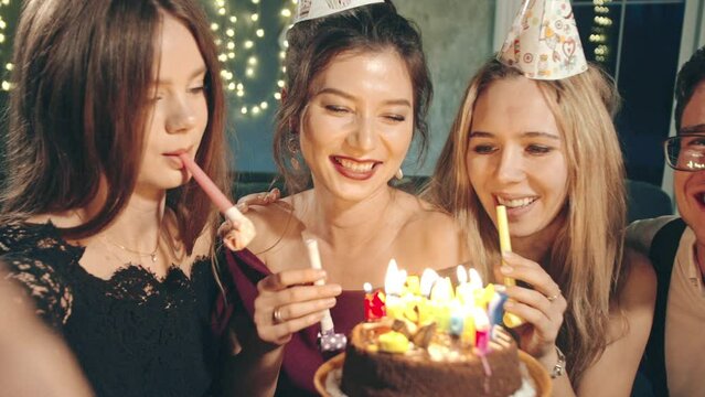 Happy multiracial friends selfie congratulating with birthday excited asian girl, giving cake, celebrating. Funny guys in holiday or birthday caps resting together, laughing, blowing whistle at party.