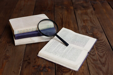 Stack of antique books with magnifying glass on wooden table