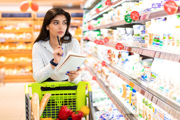 Woman With Shopping List Calculating Prices Buying Groceries In Supermarket