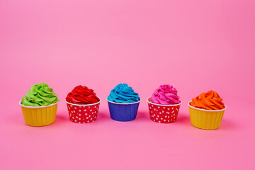 A row of colorful cupcakes on a pink background.