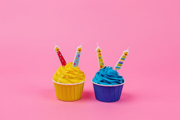 A row of colorful cupcakes with candles on a pink background.
