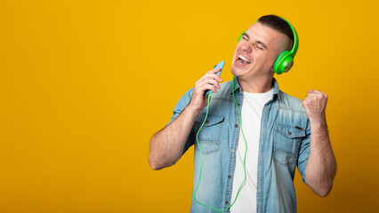 Banner copy space. Happy man with earphones holding smartphone isolated on yellow background.