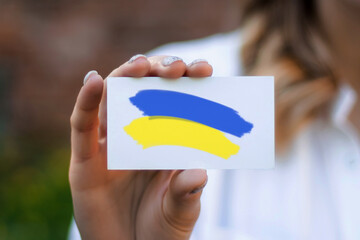 female hand shows a business card with a picture of the flag of Ukraine on a background of nature. Business and work in Ukraine
