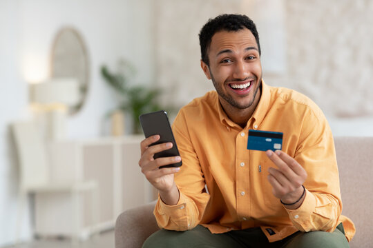 Smiling guy using phone and credit card at home