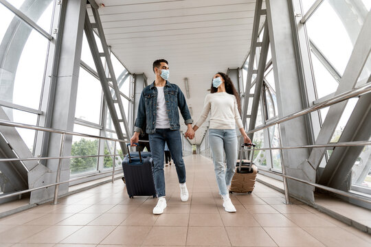 Young Arab Couple In Medical Masks Walking With Suitcases At Airport Hallway