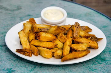 Home-made fries on a plate with some mayonaise on a round table