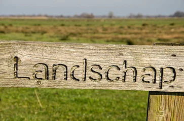 Foto auf Leinwand Wooden board with the word "landschap" (Dutch for landscape) carved into it, in a Dutch polder landscape with meadows all the way to the horizon © Frans