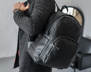 A man holds a black leather backpack on one shoulder. Man's hand with a backpack behind. Business...