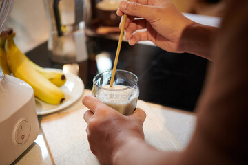 Hands of man putting hygienic, safe, and organic bamboo drinking straw in glass of smoothie
