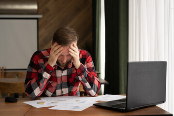 Portrait of a tired nervous bearded businessman in casual clothes working in a cafe, sitting with a...