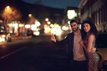 Time to go home. Shot of a cheerful young couple holding each other while waiting for a taxi outside in the streets at night.