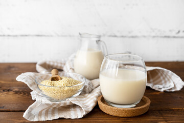 Millet milk in glass, jar and bowl on brown wooden table with withe wooden backside