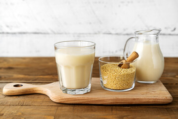 Millet milk in glass, jar and bowl on cutting board with wooden background