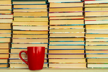 hundreds books in Stacks and red cup stands on Books Inside Background. relax time with tea and Books That Can Be Read for Life. Many Multicolored Books In Columns
