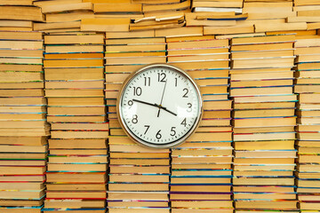 Many books in stacks and white big round clock hang on in the middle of books inside background. Time and books that can be read for life. Many multicolored books in columns