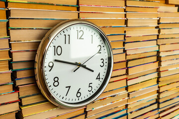 Many books in stacks and white big round clock hang on books inside background. Time and books that can be read for life. Many multicolored books in columns